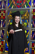 graduate holding her diploma in front of a stained glass window