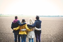 teens standing together in a field with backs to the camera 