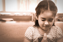 Girl with eyes closed and clasped hands in prayer.