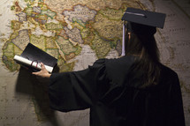 graduate pointing to a world map in her cap and gown