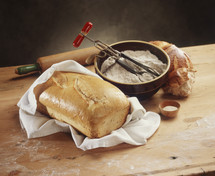 Loaf of handmade bread on a wooden table with a bowl of flour and a rolling pin
