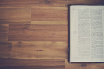 edge of an open Bible on a wood floor 
