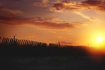 sunset over a beach and fence line on the dunes 