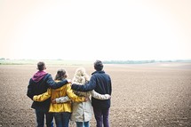 teens standing together in a field with their backs to the camera 