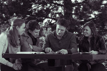 college students reading their Bibles outdoors at a picnic table during a Bible study