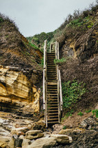 Wooden stairs leading down rocky hills to the beach.