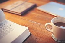 Bible opened to Genesis on a desk, coffee mug, and journal 