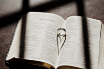 wedding band in the pages of a Bible forming a heart shadow