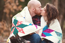 Couple wrapped in a quilt kissing.