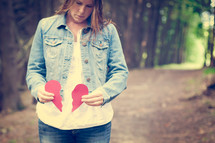 Woman standing on a trail outside holding the pieces of a broken heart.