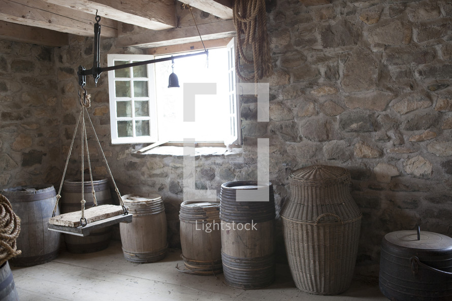 Baskets, barrels, and a pulley in a stone room with wooden floor.