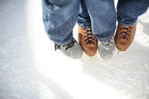Two pairs of feet wearing ice skates.