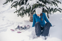 woman sitting in snow next to skis 