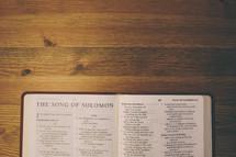 Bible on a wooden table open to the book of the Song of Solomon.