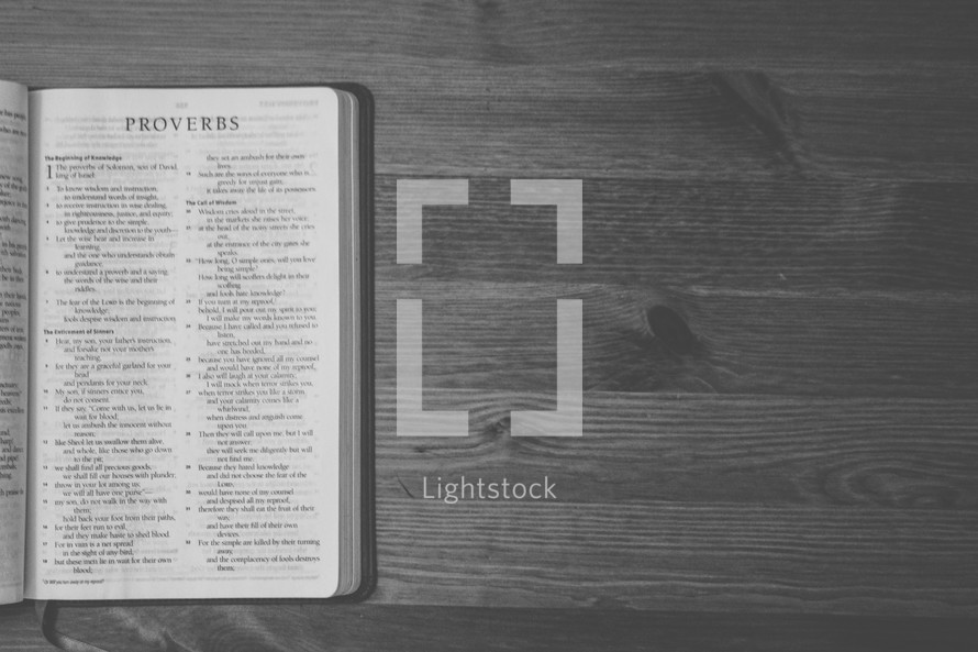 Bible on a wooden table open to the book of Proverbs.
