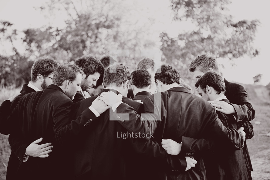 men in suits in a group prayer
