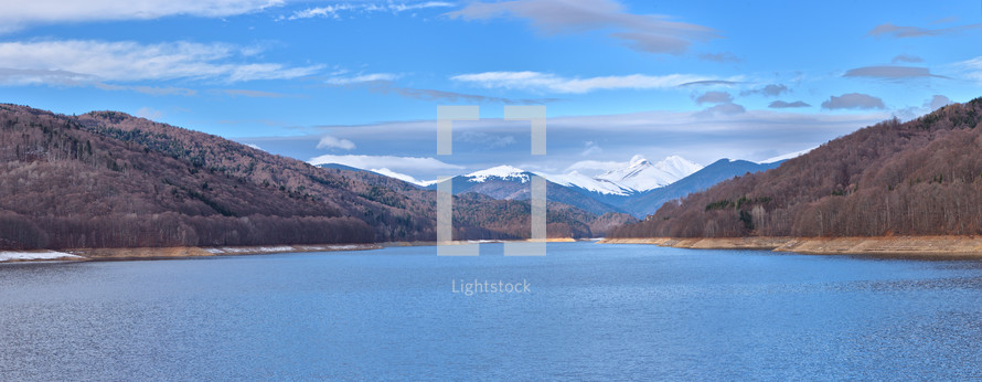Mountain lake panorama against cloudy sky and mountains covered with snow