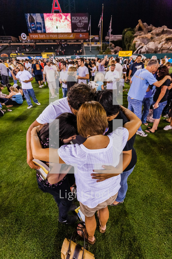 Family in a huddle on baseball field praying salvation crusade holding hugging love trust