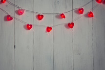 String of heart-shaped lights on a white wood background.