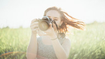a teen girl holding a camera in a field 