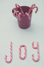 Candy canes in a red cup and spelling "joy".