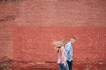a couple walking holding hands in front of a red brick wall 
