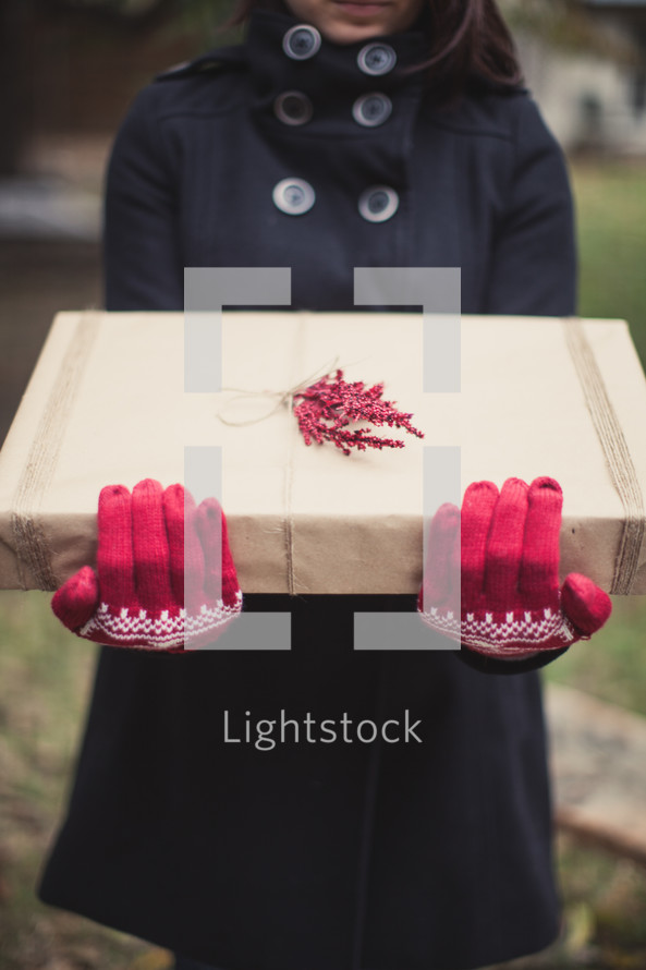 A woman wearing red gloves holding a gift wrapped in brown paper