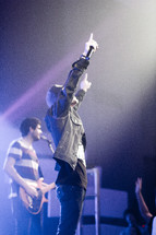 Man with arms raised on stage during a concert performance.