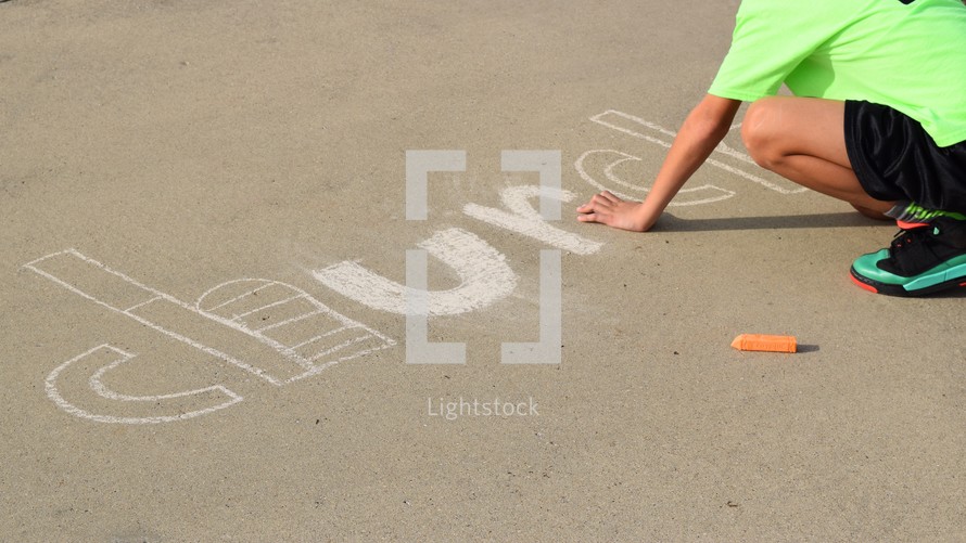 a little boy drawing the word church on concrete with sidewalk chalk 