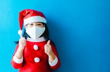 a chid in a Santa Suit putting on a face mask 