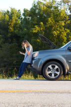 a woman on the phone next to a broken down vehicle 