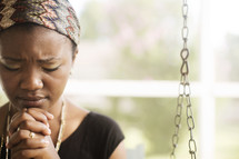 African-American teen sitting outside on a porch swing praying.