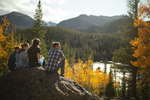 young adults sitting on a rock looking out at a lake in fall 