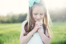 a little girl praying outdoors 