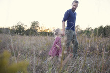father and daughter walking through tall grasses holding hands 