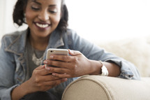 An African American woman sitting on a couch checking her cellphone 