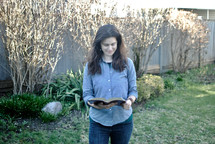A woman standing outside reading the Bible