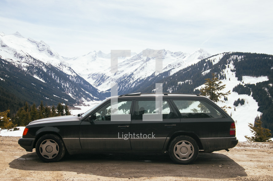 a parked station wagon in front of snow capped mountains 