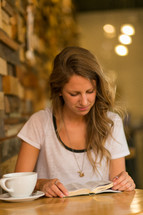 woman sitting at a table in a cafe reading a Bible