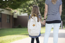 A mother and daughter holding hands and looking at a school.