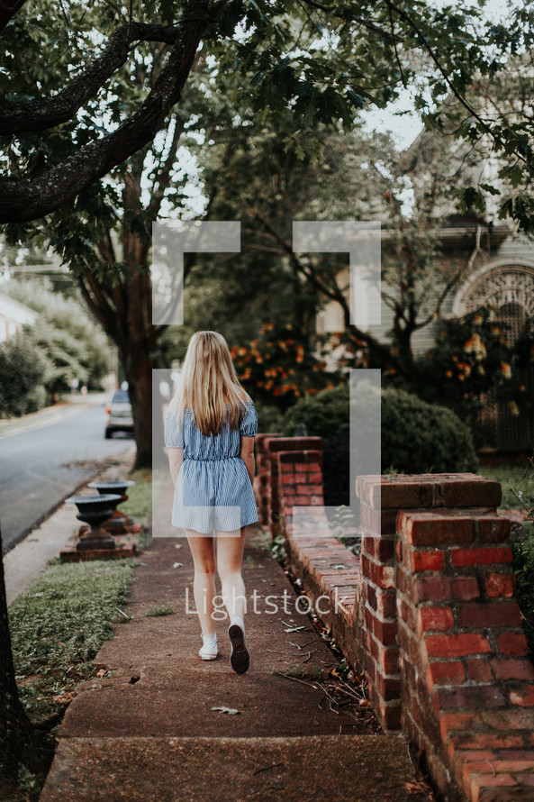 teen girl walking down a neighborhood sidewalk 