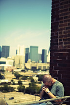 A white, young adult man praying on top of a building