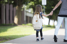 A mother and daughter holding hands and walking to school.