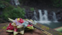 Canang Sari Daily Offerings made by Balinese Hindus with Taman Sari Waterfall and Natural Pool on The Background