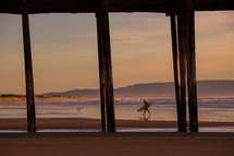 surfer walking under a pier 