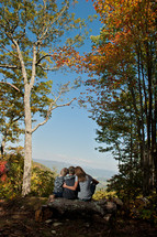 family sitting on a fallen tree overlooking a mountain valley