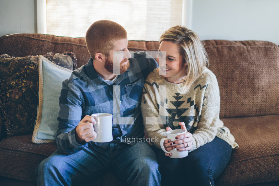 couple sitting on a couch drinking hot cocoa together 