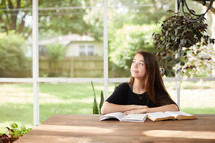 a teen girl reading and looking away thinking at her home