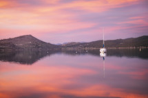 Pink Clouds and a lone sailboat reflect in Carter Lake's waters, located in Loveland Colorado on a beautiful spring morning