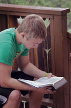 young man reading a Bible on a porch 